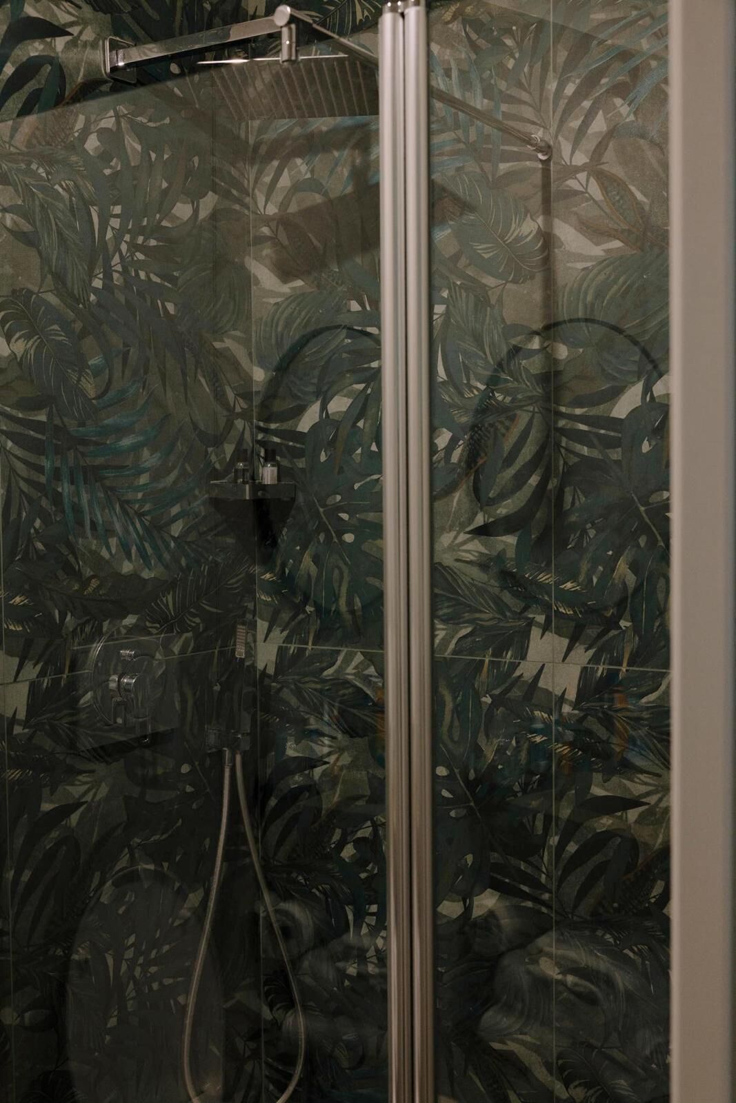 A shower with a glass door and a tropical leaf pattern on the walls.