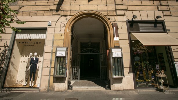 Fachada de edificio con un gran arco de entrada, maniquíes en el escaparate y un letrero que dice 'TWIN-SET'.
