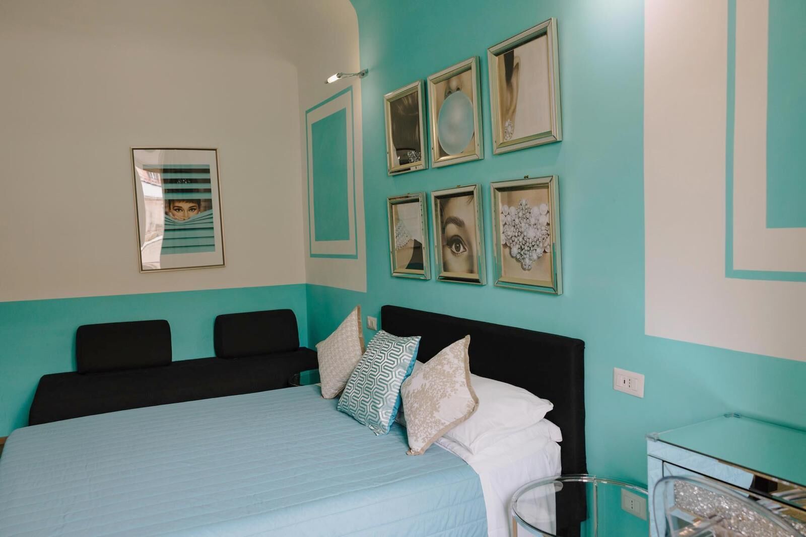 Una camera da letto con un letto, due sedie, un comodino e una parete decorata con quadri.