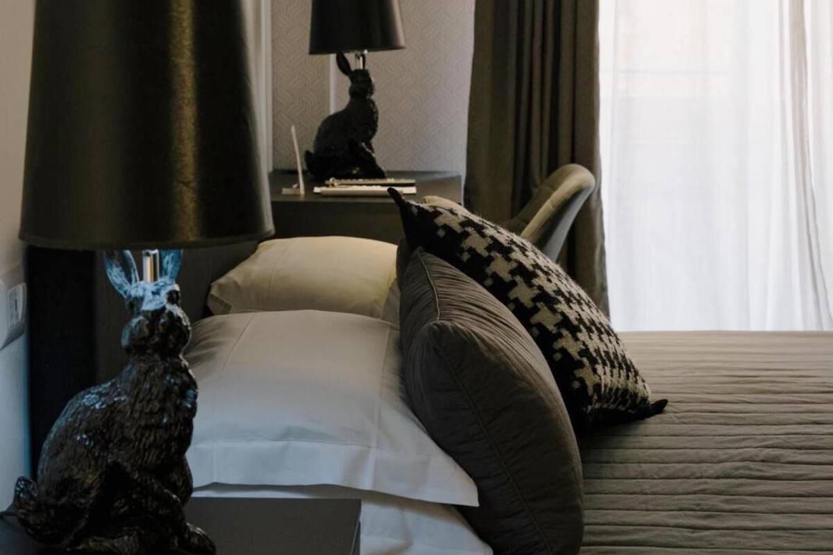 A hotel room with a bed, a nightstand with a lamp, a decorative rabbit figurine, and a wall with framed pictures.