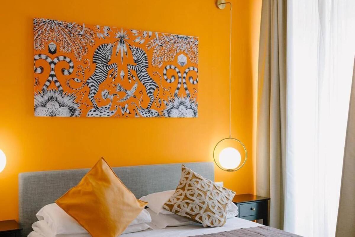 A hotel room with a large bed, two bedside tables, a wall-mounted artwork, and a window with curtains.