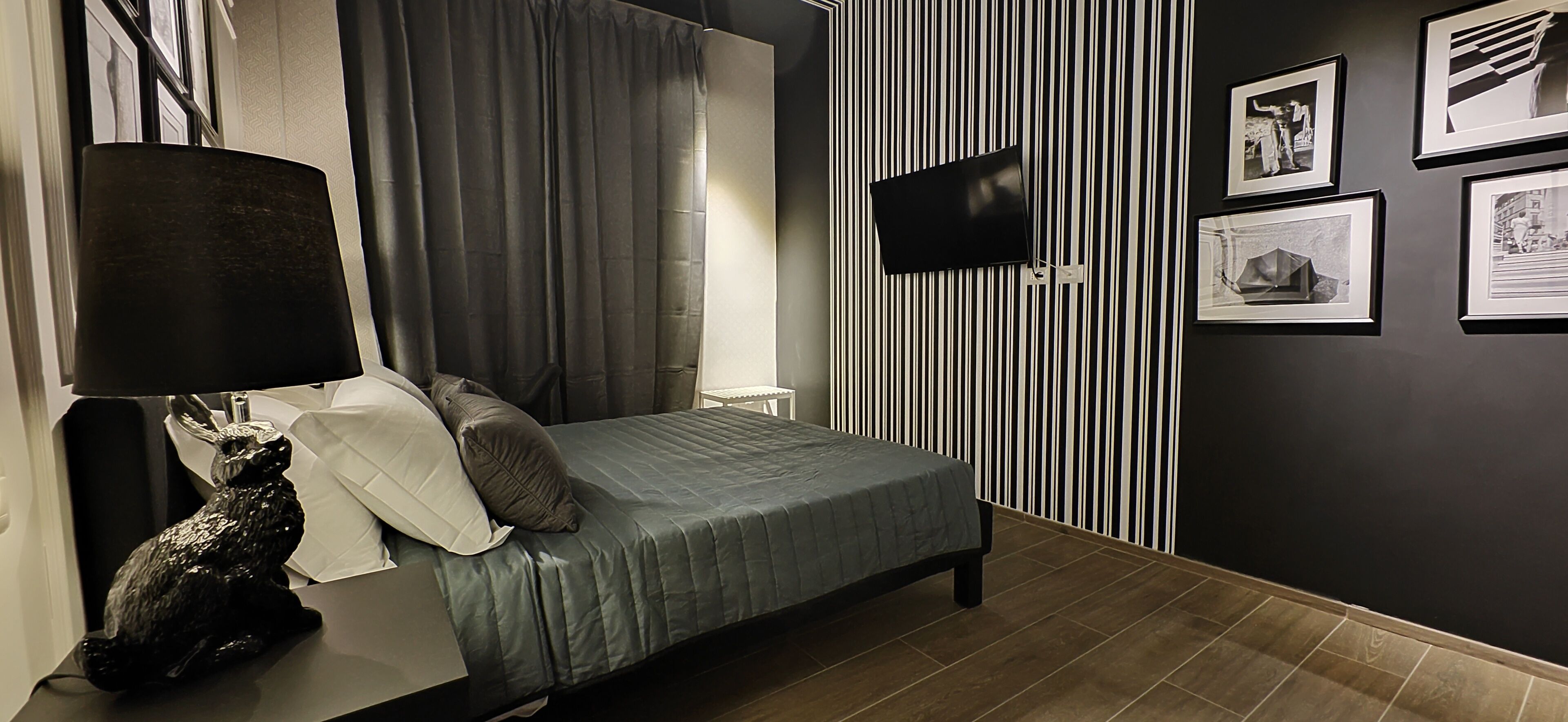 A modern bedroom with a bed, a nightstand, a lamp, a wall-mounted TV, and framed pictures.