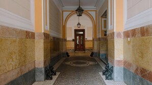 Un pasillo con suelos de mármol estampado, una puerta de madera al final y dos estatuas a cada lado.
