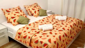 A neatly made bed with a watermelon-patterned bedspread, a small bedside table, and a nightstand. - Beautiful villa on the beach (Sevid)