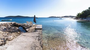 A clear waterfront with a stone jetty, a row of beach chairs, and a small boat. - Beautiful villa on the beach (Sevid)