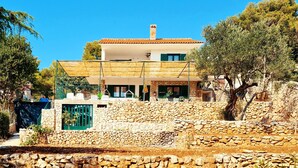 A two-story stone house with a tiled roof, a stone wall in front, and a tree to the right. - Beautiful villa on the beach (Sevid)