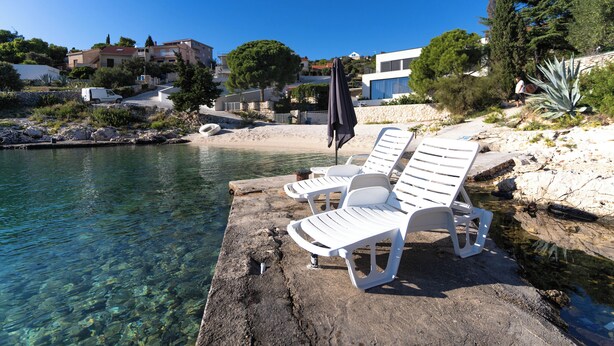 A clear waterfront with white lounge chairs and a rocky edge. - Beautiful villa on the beach (Sevid)