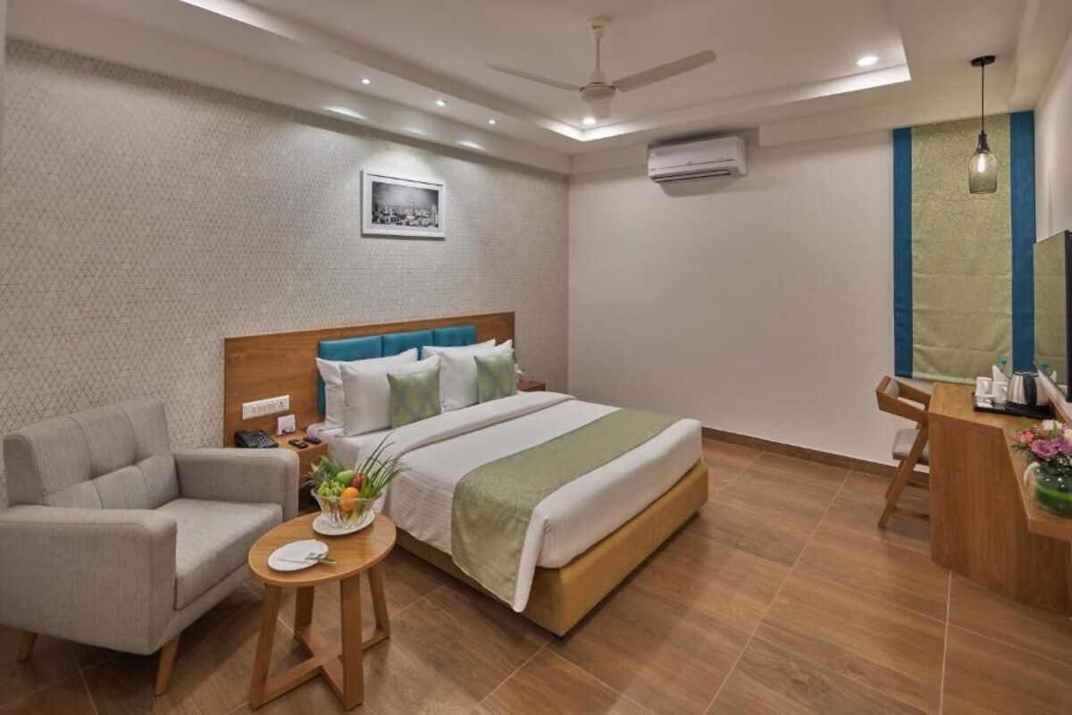 A hotel room with a bed, a sofa, a small table with a plant, and a desk with a chair.