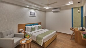 Une chambre d’hôtel moderne, équipée d’un lit, d’un canapé, d’une petite table avec un panier de fruits et d’un bureau avec une chaise.
