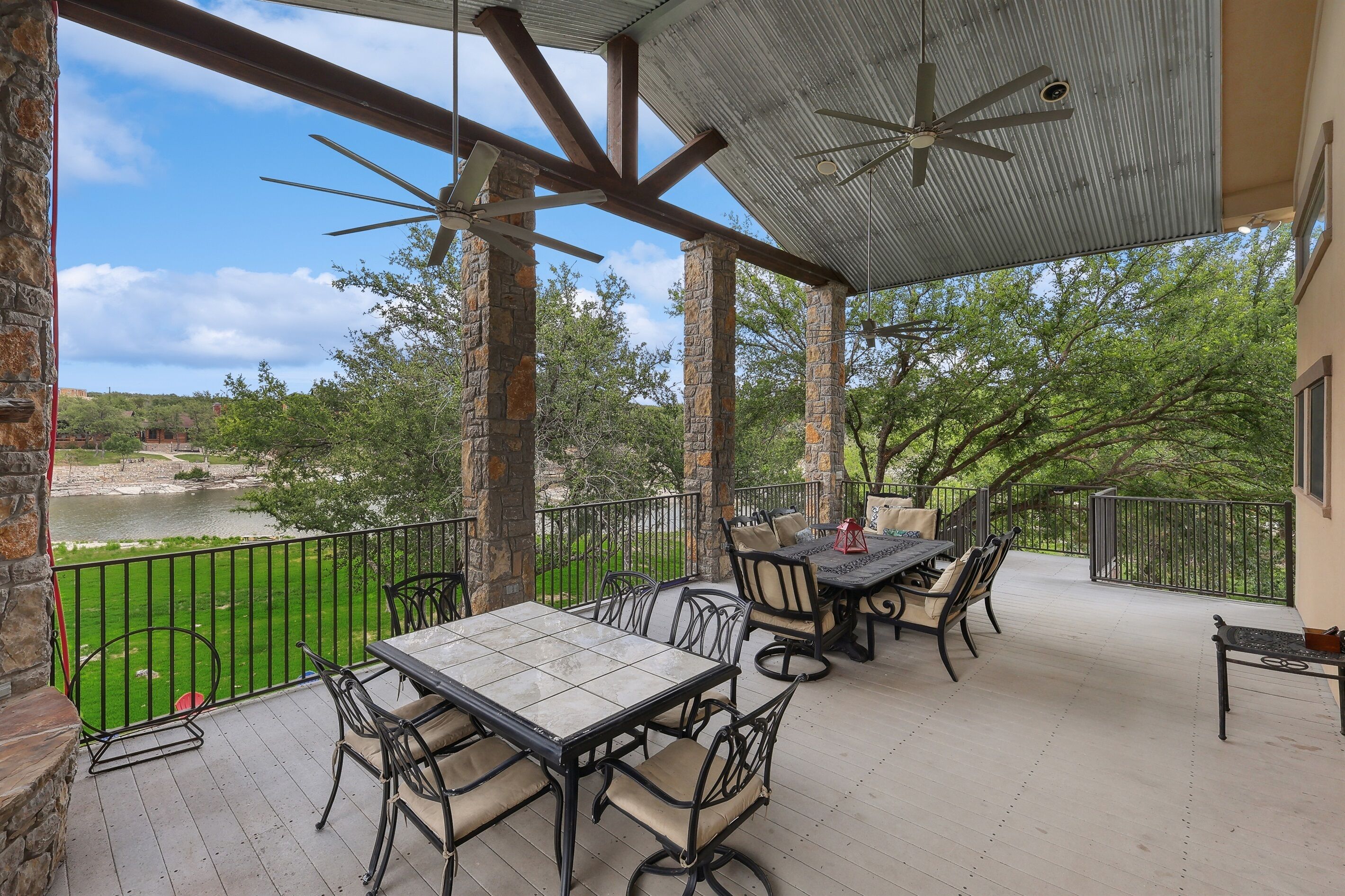 A covered outdoor patio with a table and chairs, overlooking a river and greenery.