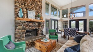 A spacious living room with a stone fireplace, green armchairs, a wooden coffee table, and a large sofa.