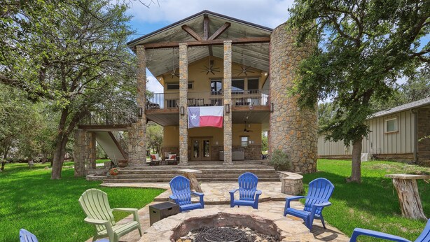 A two-story stone building with a balcony, outdoor seating area with chairs, and a flag.