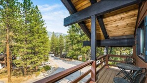 Terraza de madera con sillas metálicas, con vista a una zona boscosa bajo un cielo despejado.