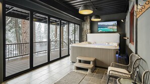 Zona de spa con un jacuzzi, sillas de mimbre y un amplio ventanal con vistas a un paisaje nevado.
