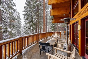 Une terrasse en bois dotée d’un sol en pierre, entourée d’arbres couverts de neige.