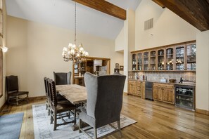 Un vaste espace dédié à la salle à manger, avec une table et des chaises en bois, un lustre et une cuisine dotée de meubles en bois et d’un lave-vaisselle.