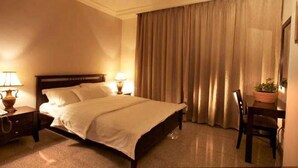 A hotel room with a bed, two bedside lamps, a chair, and a potted plant. - Tamrah Suites Hotel (Amman)