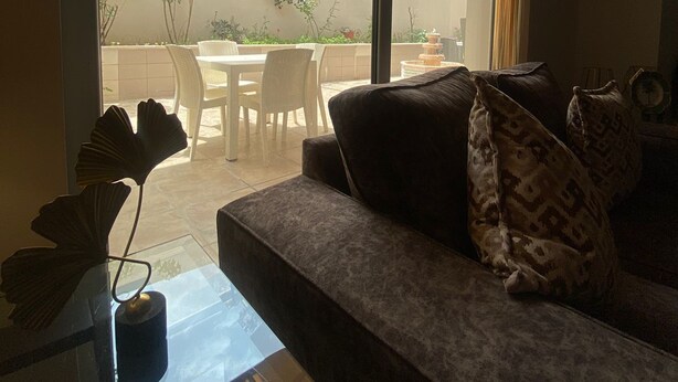 A living room with a sofa, a glass coffee table, and a view of an outdoor patio with a table and chairs. - Tamrah Suites Hotel (Amman)