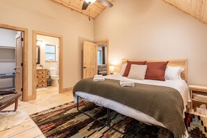 Un dormitorio con cama, cabecera de madera, mesitas de noche, alfombra y techo de madera.