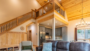 Un espacio habitable amplio con un sofá de cuero marrón, un sillón gris claro y una escalera de madera que conduce a un nivel superior.