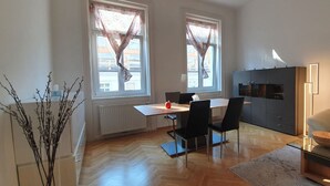 A modern, well-lit room with a wooden floor, a dining table with chairs, a sofa, and a cabinet. - Servicierte Wohnung in der City (Vienna)