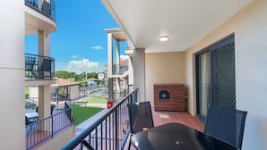 A balcony with a table and chairs, a pool in the background, and a view of neighboring buildings. - 202 South Pacific, Pacific Drive (Port Macquarie)