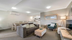 Un salon moderne avec un canapé gris, une table d’appoint en bois, un fauteuil vert et un coin repas comprenant une table et des chaises en bois.