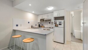 Une cuisine moderne avec des meubles blancs, un îlot central doté de tabourets, un four à micro-ondes encastré et un réfrigérateur orné d'aimants.