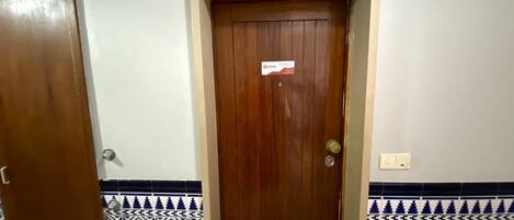 A wooden door with a sign above it, a tiled wall with a geometric pattern, and a light switch on the wall.