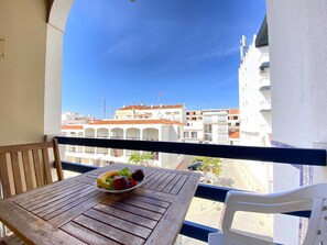 A balcony with a wooden table and a bowl of fruit, overlooking a row of buildings with red-tiled roofs. - Monte Gordo Beach I by Homing (Vila Real Santo Antonio)