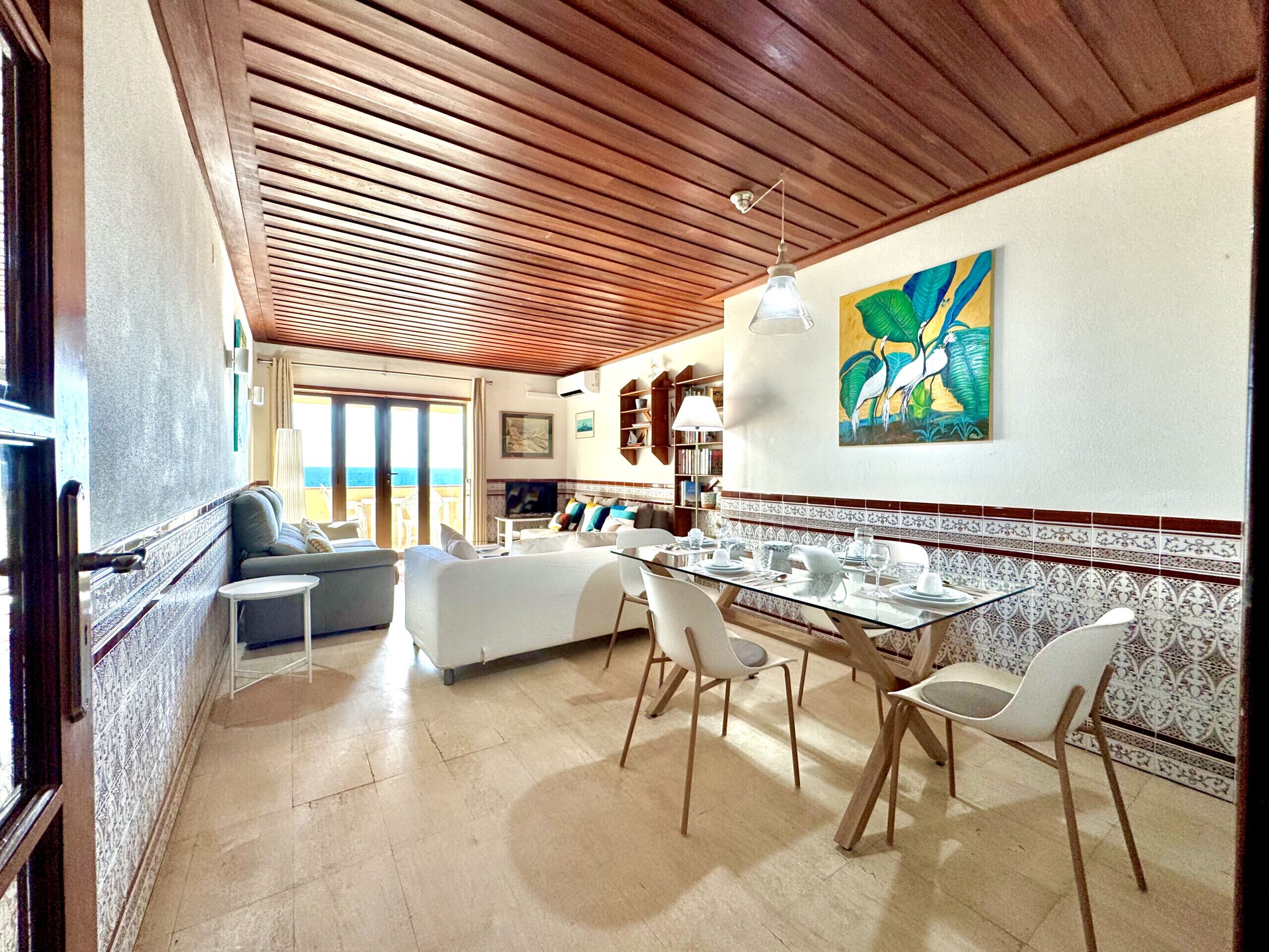 A spacious living area with a dining table set for four, a sofa, and a view of the ocean.