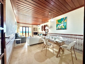 A spacious living area with a dining table set for four, a sofa, and a view of the ocean. - Monte Gordo Beachview 2 by Homing (Vila Real Santo Antonio)