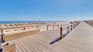 En träpromenad som leder till en strand med parasoller och en livboj.