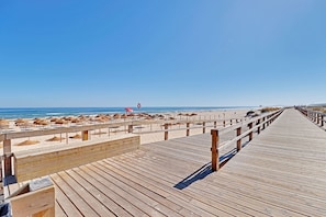 A wooden boardwalk leading to a beach with umbrellas and a lifebuoy. - Monte Gordo Beachview 2 by Homing (Vila Real Santo Antonio)