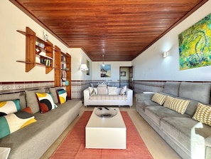 A living room with a wooden ceiling, two sofas with patterned cushions, a white coffee table, and a bookshelf. - Monte Gordo Beachview 2 by Homing (Vila Real Santo Antonio)