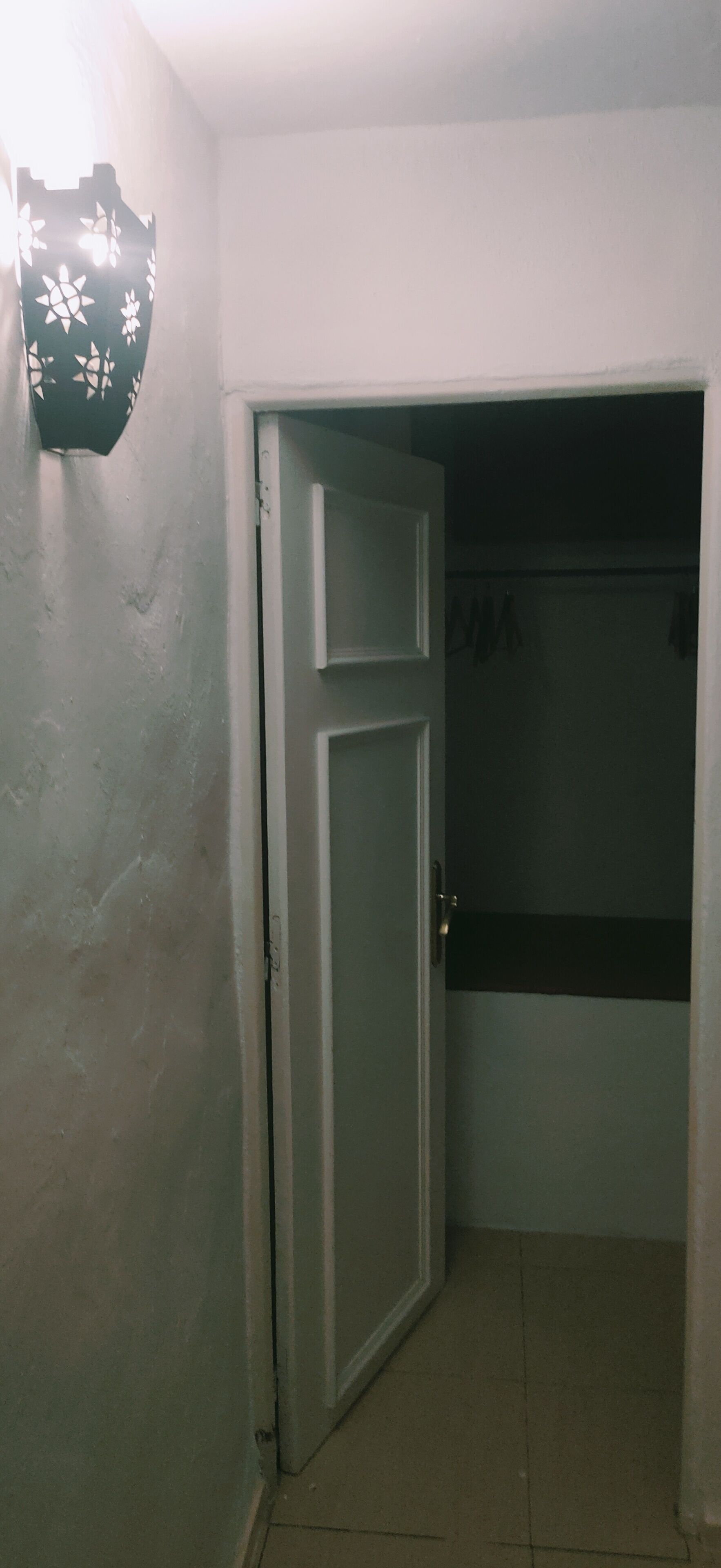 A hallway with a closed door, a light fixture on the wall, and a tiled floor.