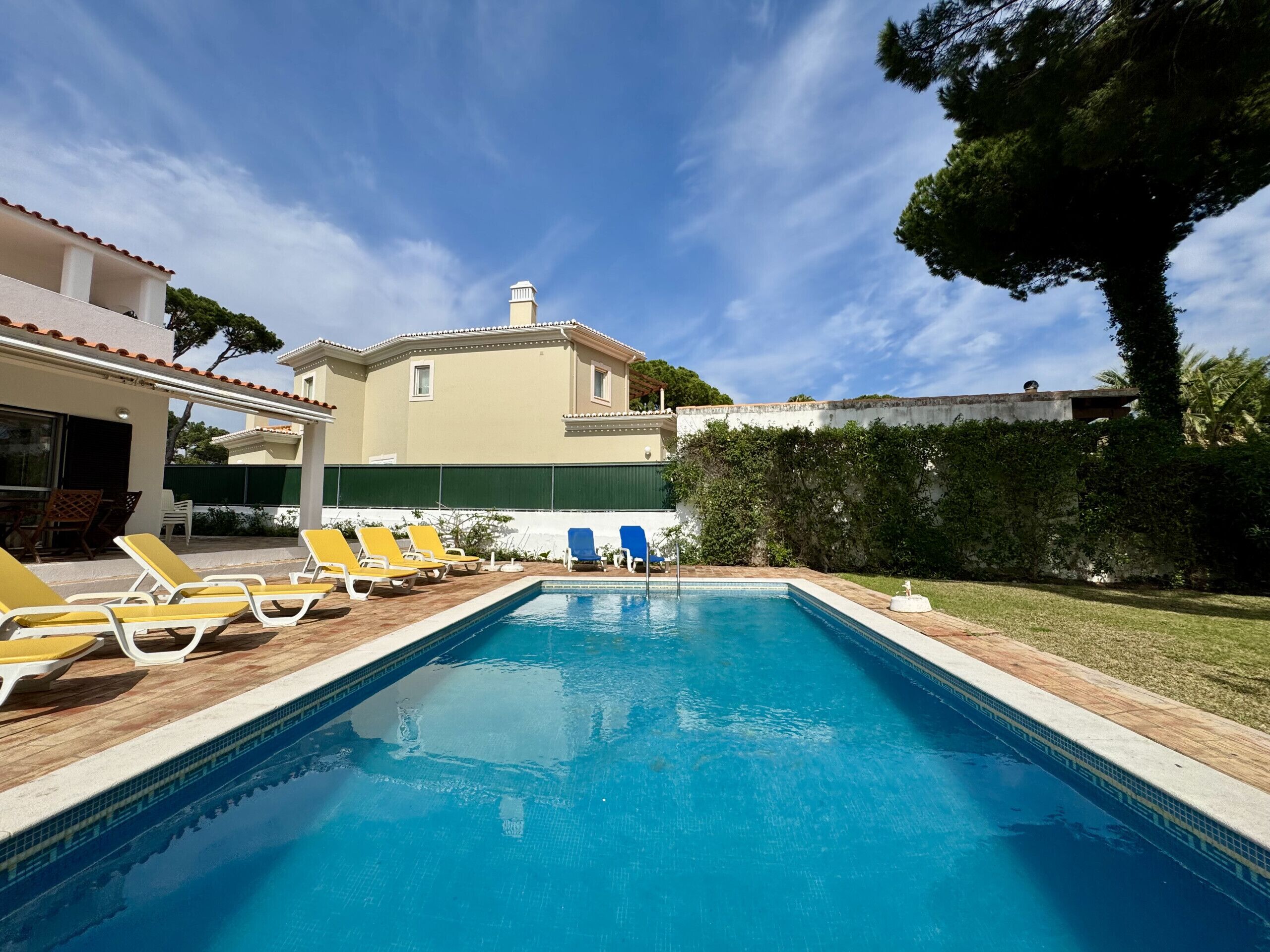 A swimming pool with lounge chairs, a building with a tiled roof, and a clear sky.