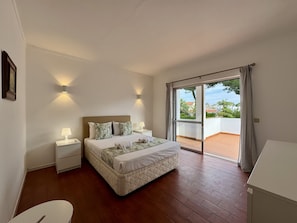 A bedroom with a bed, bedside tables, a view through a sliding glass door, and a white wall. - Vilamoura Ocean Villa With Pool (Loulé)