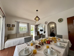 A dining area with a table set for breakfast, a sofa, and a view of the outdoors. - Vilamoura Ocean Villa With Pool (Loulé)