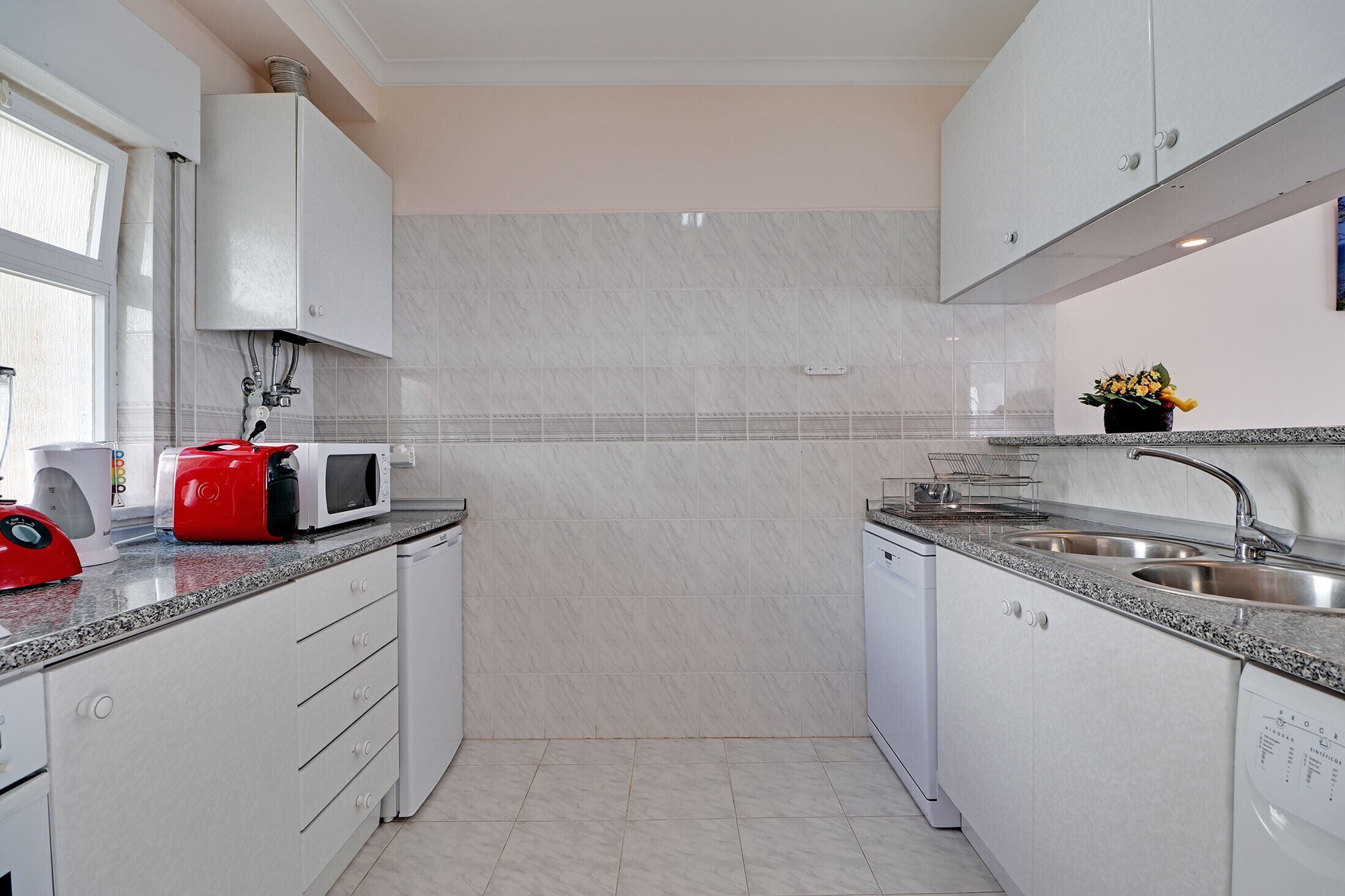 A modern kitchen with white cabinets, a granite countertop, a microwave, a sink, and a dishwasher.