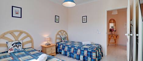Un dormitorio con dos camas, una mesita de noche, una lámpara y una puerta que da a un baño.