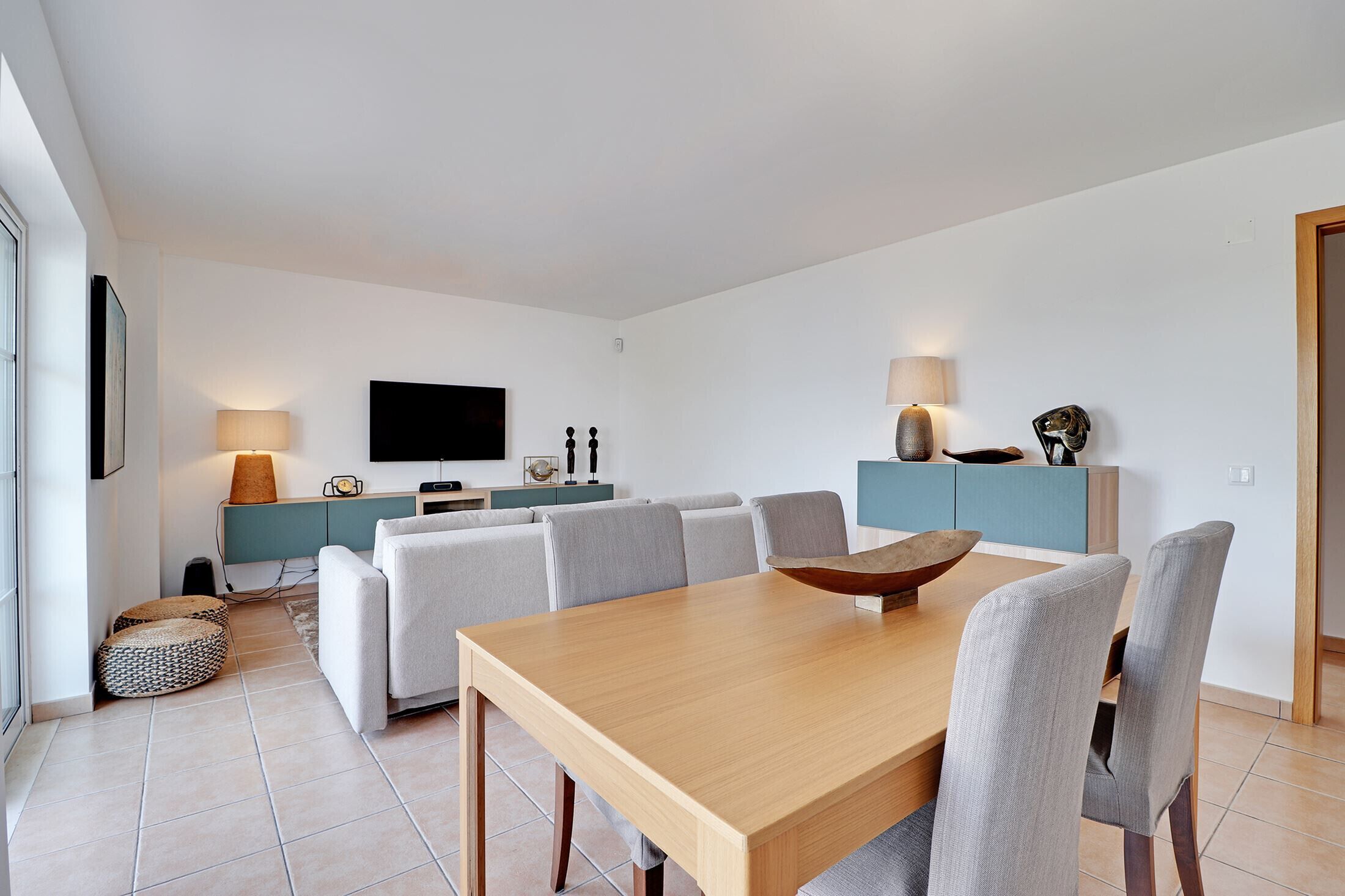 A modern living room with a wooden dining table, grey sofas, and a blue cabinet.