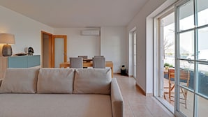 A modern living room with a sofa, a dining table with chairs, a lamp, and a sliding glass door leading to an outdoor area. - Tavira Formosa BAY 1 by Homing (Tavira)