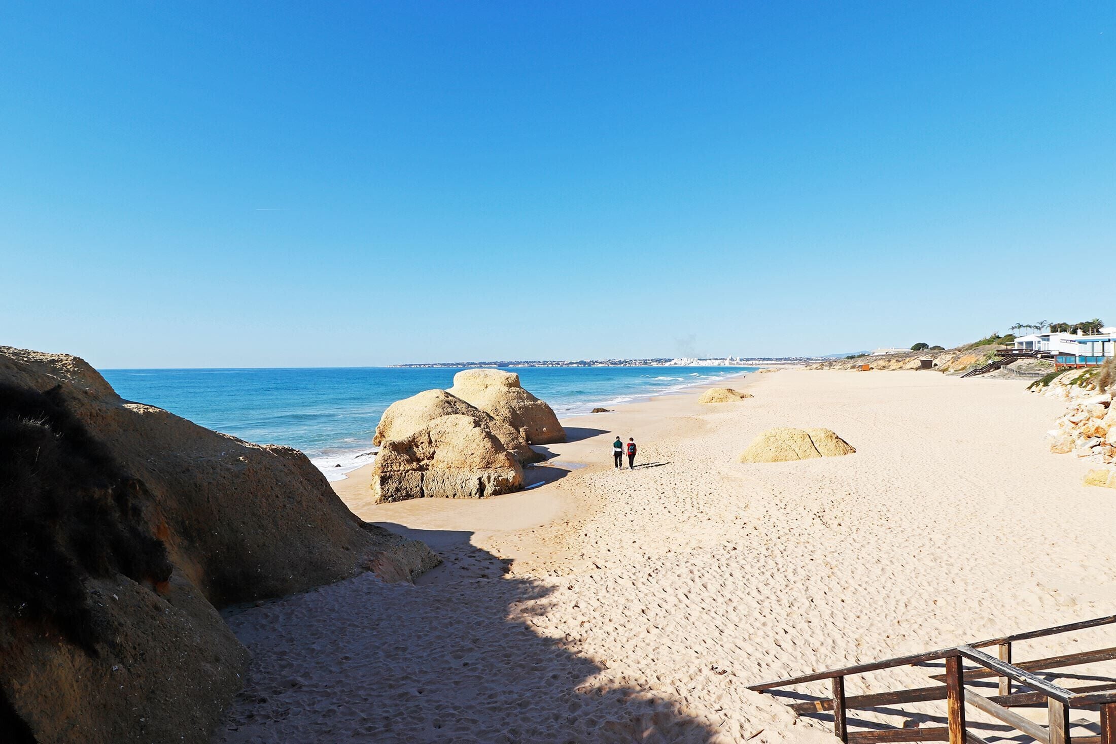 A sandy beach with large rocks and a clear blue sky.