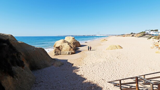 A sandy beach with large rocks and a clear blue sky.