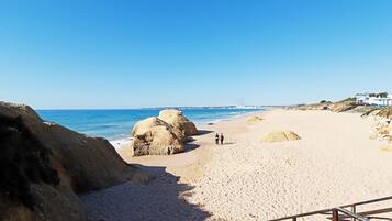 A sandy beach with large rocks and a clear blue sky.