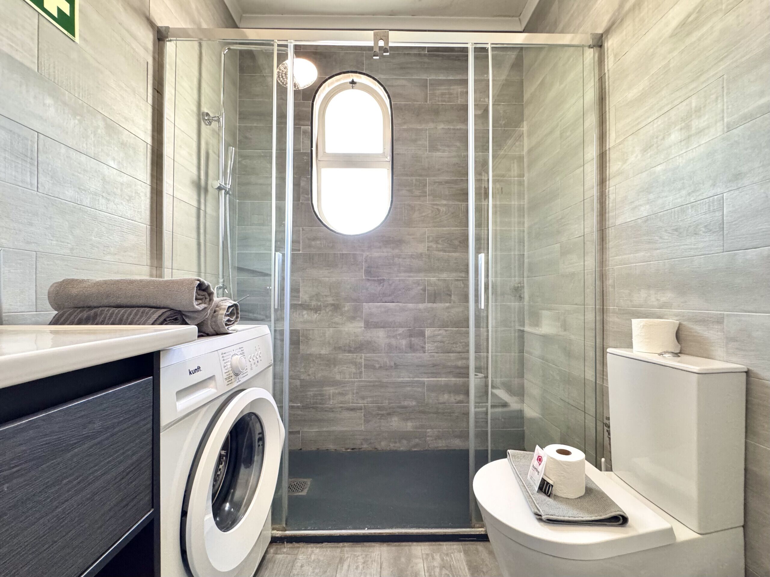 A compact bathroom with a glass-enclosed shower, a washing machine, and a toilet.