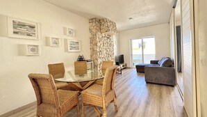 A modern living room with a glass-top dining table surrounded by wicker chairs, a stone accent wall, and a grey sofa.