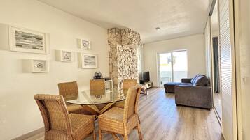 A modern living room with a glass-top dining table surrounded by wicker chairs, a stone accent wall, and a grey sofa.