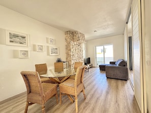 A modern living room with a glass-top dining table surrounded by wicker chairs, a stone accent wall, and a grey sofa. - Albufeira Delight With Pool by Homing (Albufeira)